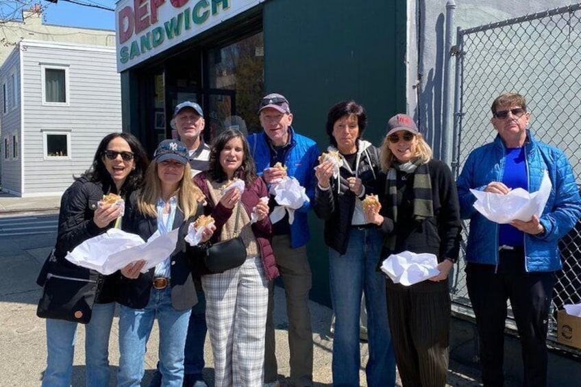 A group of people standing in front of a sandwich shop. 5