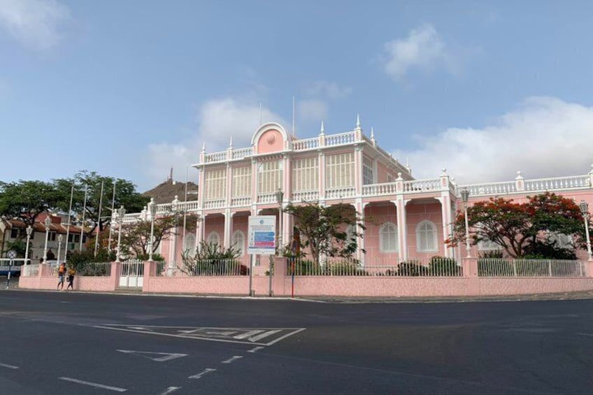A pink colonial-style building with a white fence and trees in the foreground. 5