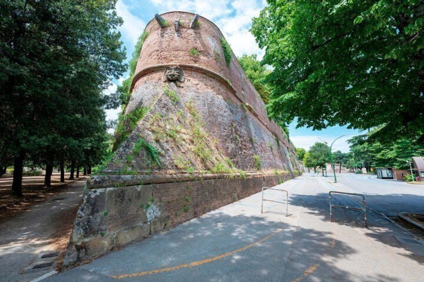 A large, cylindrical brick structure with a conical base, surrounded by trees and a paved road. 5