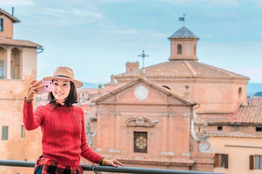 A person in a red sweater and hat taking a selfie with a historic building in the background. 1