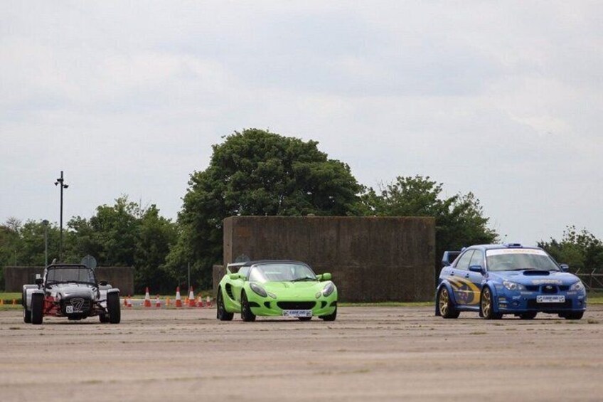 Three sports cars parked on a concrete surface with a fence and trees in the background. 2