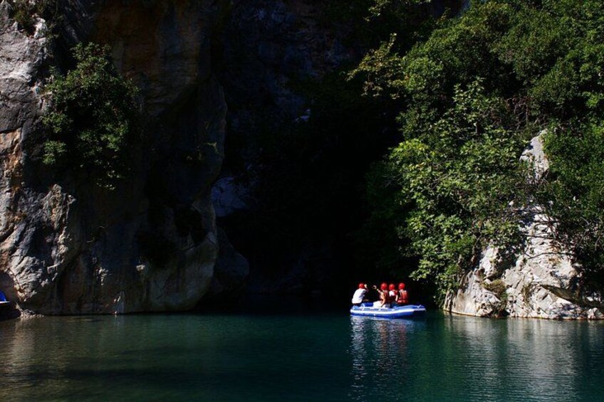 A group of people in a blue raft on a calm river surrounded by rocky cliffs and greenery. 2