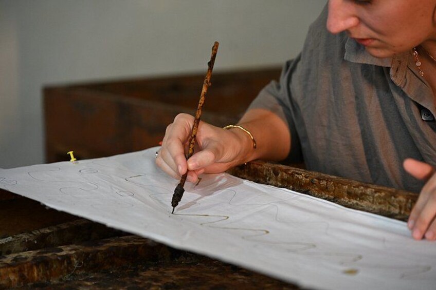 A person drawing on a large sheet of paper with a stick. 1