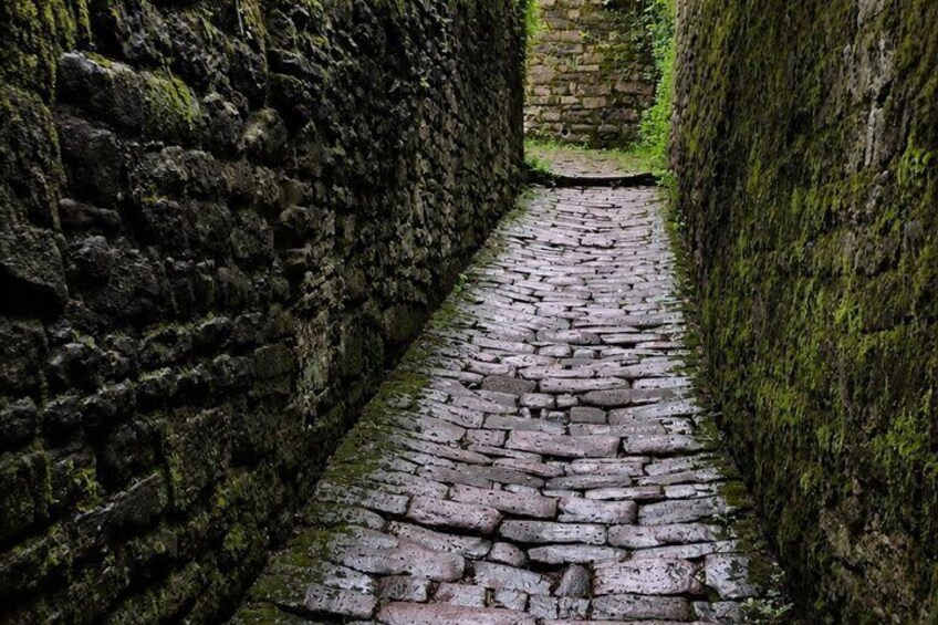 A narrow cobblestone path flanked by moss-covered stone walls. 3