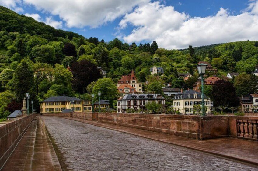 A cobblestone bridge, lush green hills, and historic buildings. 2