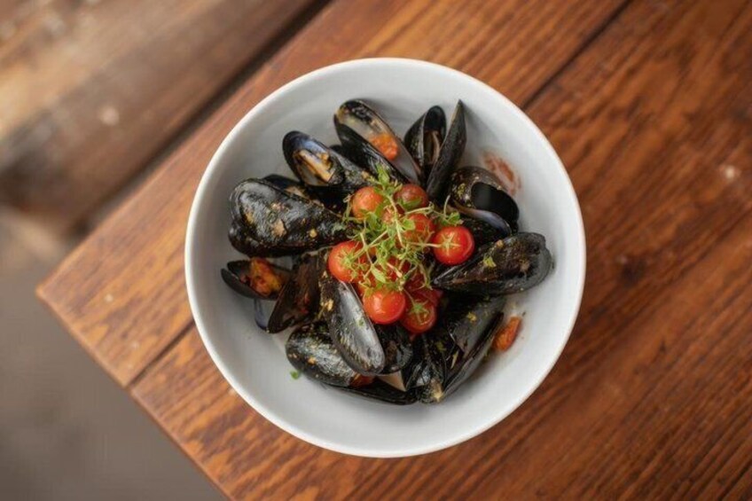 A bowl of mussels garnished with cherry tomatoes and herbs on a wooden table. 5