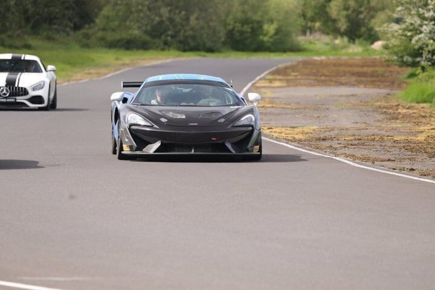 A grey sports car on a road with a white car ahead. 4