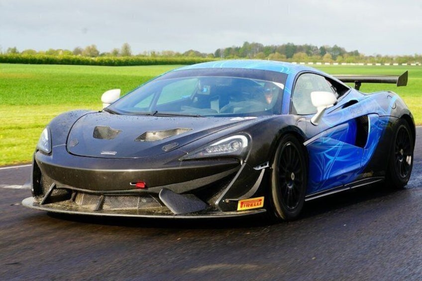 A sports car on a wet road with a green field in the background. 1