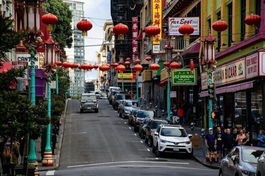 A street lined with parked cars, red lanterns, and various storefronts. 1