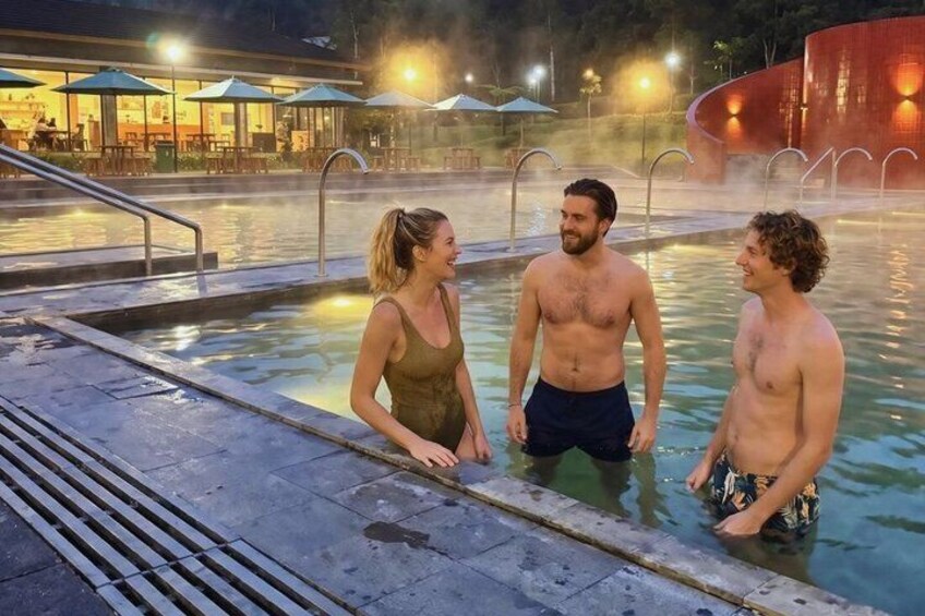 A swimming pool with people standing in it, surrounded by outdoor seating and a building in the background. 5