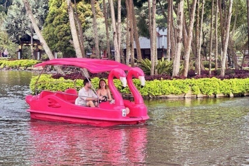 A pink boat with a flamingo design on a calm body of water, surrounded by lush greenery and trees. 3
