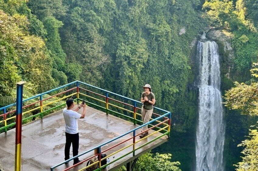A person taking a photo of a waterfall from a platform with a railing. 1