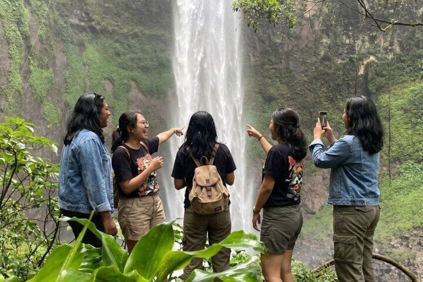 A group of people observing a waterfall in a forested area. 2