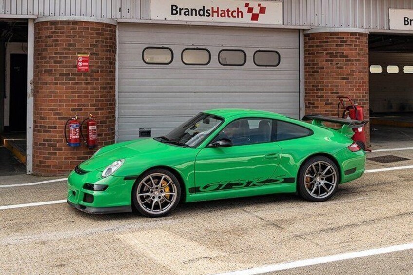 A green sports car parked in front of a garage with a fire extinguisher on the wall. 5
