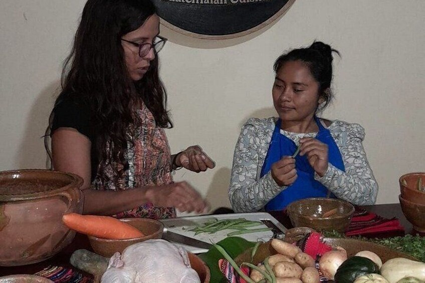 Two women at a table with various vegetables and cooking utensils. 5