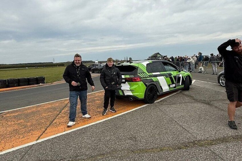 A green sports car parked on a racetrack with two people standing beside it. 3