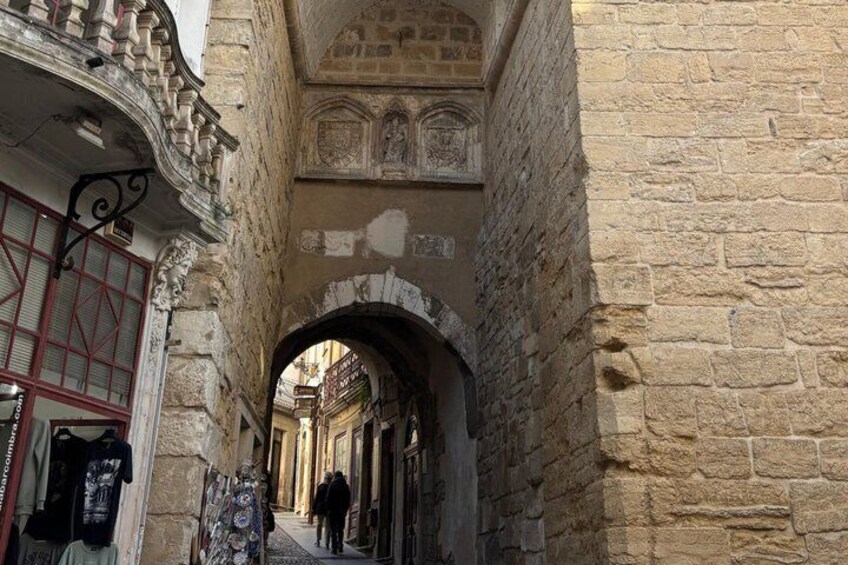 A narrow stone alleyway with an arched passageway, a shop with a red door, and a person walking away. 2
