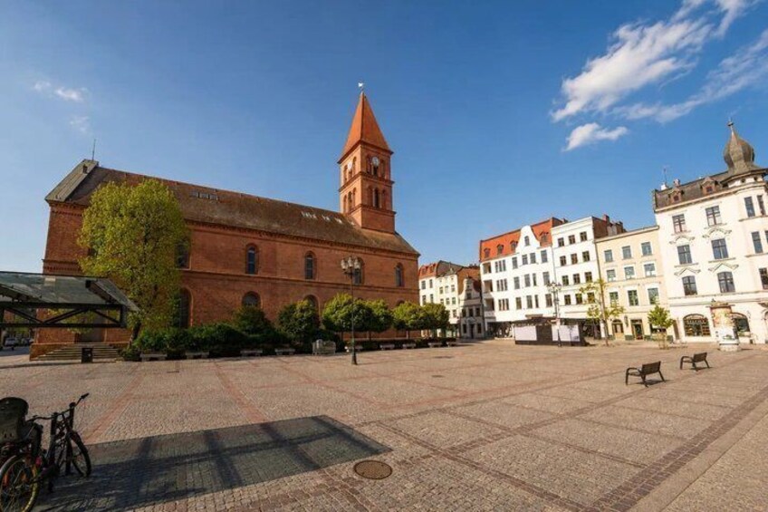 A square with a red brick building, a tower, and white buildings in the background. 2