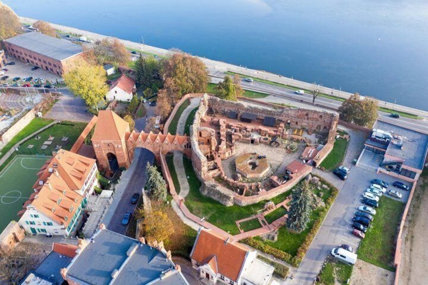 An ancient fortification with a circular wall, a central courtyard, and a modern building with a red roof. 1