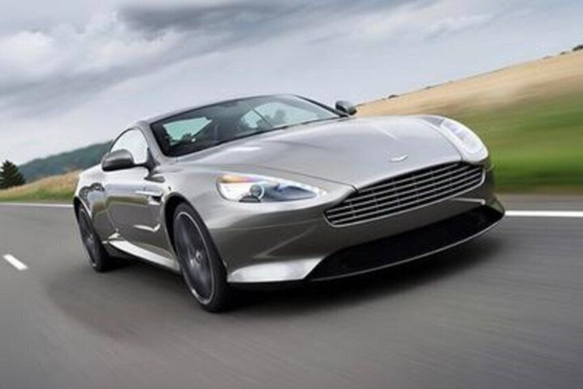 A silver sports car driving on a road with a cloudy sky in the background. 1