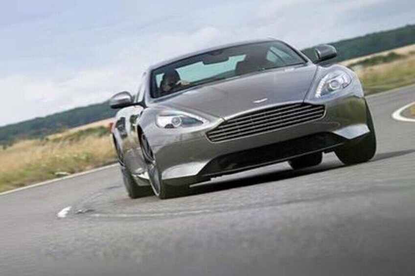 A silver sports car driving on a road with a clear sky and distant hills. 2