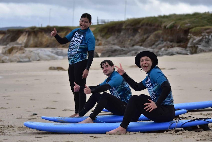 Three people on a beach with surfboards, one giving a thumbs up. 1