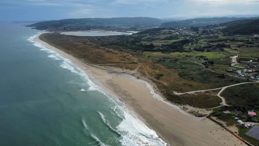 A coastal landscape with a sandy beach, a winding road, and a mix of green fields and buildings. 3