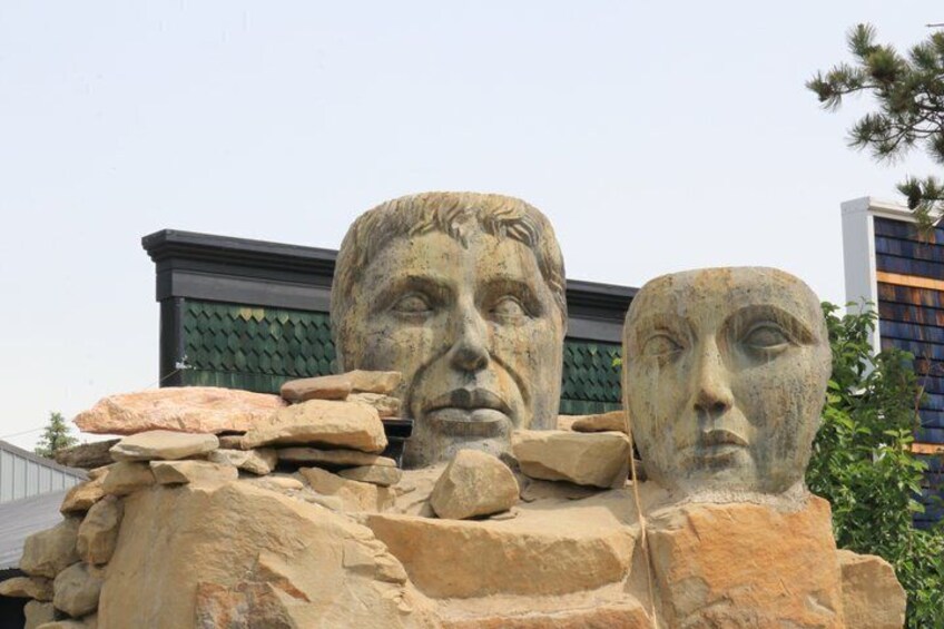 A sculpture of three heads with a building in the background. 3