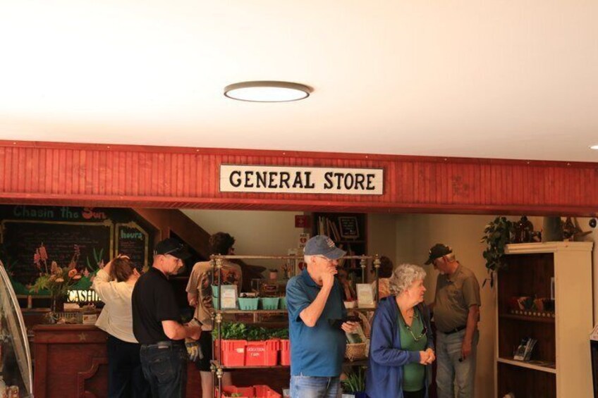 A general store interior with people browsing, a sign above the counter, and a red roof. 2