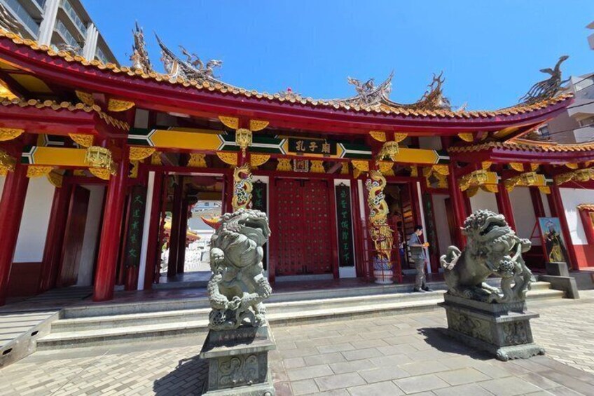 A traditional Chinese building with ornate red and gold decorations, two lion statues in front, and a clear blue sky. 3