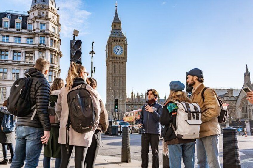 A group of people standing on a street with the Big Ben clock tower in the background. 1