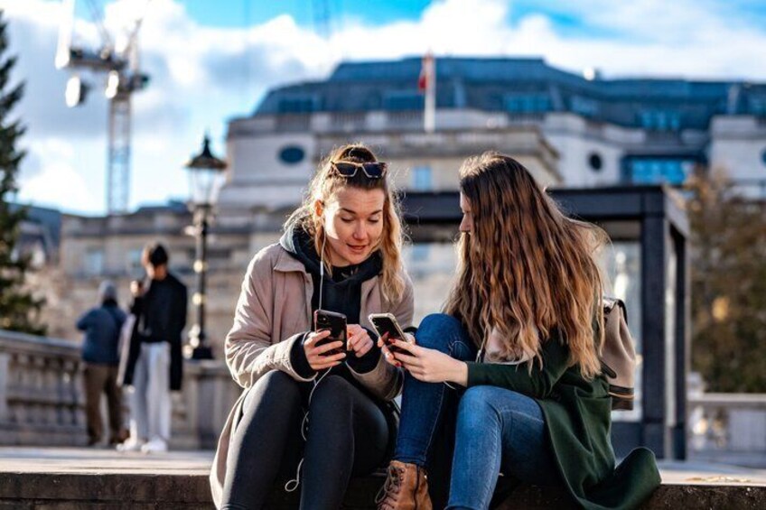 Two people sitting on a ledge, one holding a smartphone. 3