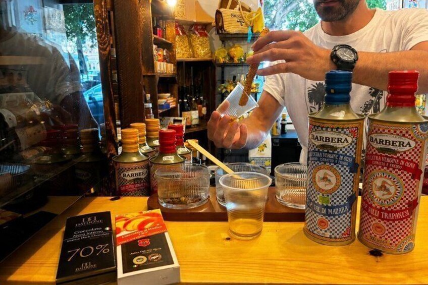 A person pouring a drink into a glass, with bottles of Barbera wine on the counter. 1