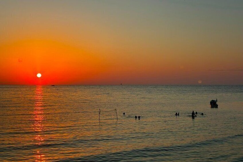 A sunset over a calm sea with a boat and people in the water. 5