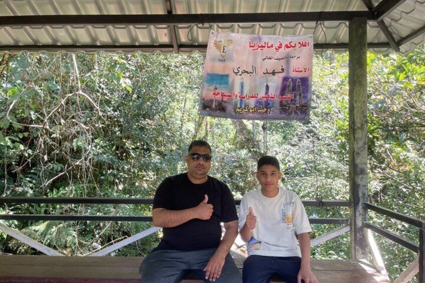 Two people sitting on a bench under a covered area with a banner in the background. 3