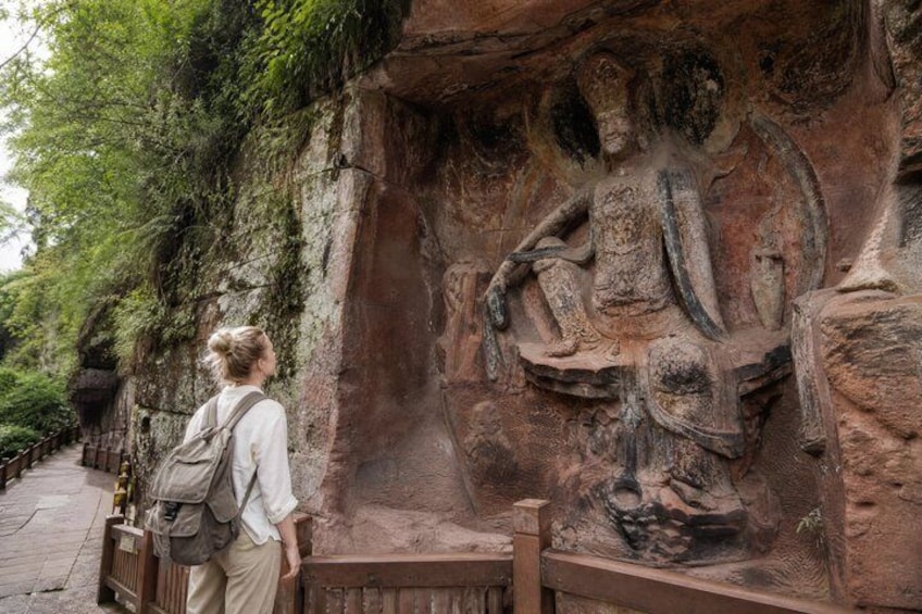 A person standing in front of a rock carving of a seated figure. 5