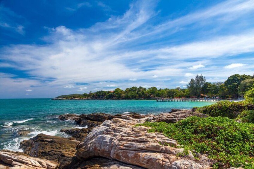 A coastal landscape with rocky shores, clear turquoise water, and a pier extending into the sea. 1