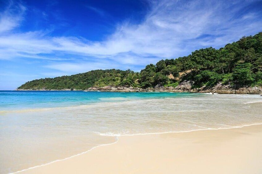 A beach with clear turquoise water, sandy shore, and a forested hill in the background. 4
