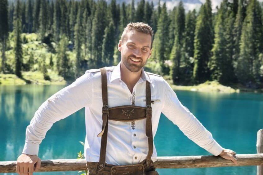 A person in traditional attire leaning on a wooden railing with a lake and forest in the background. 2