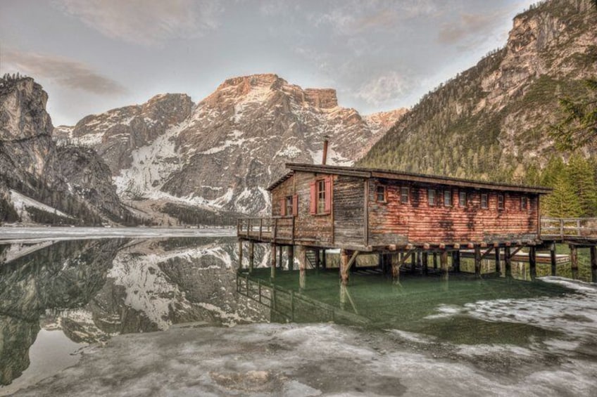 A wooden cabin on stilts over a calm lake with mountains in the background. 5