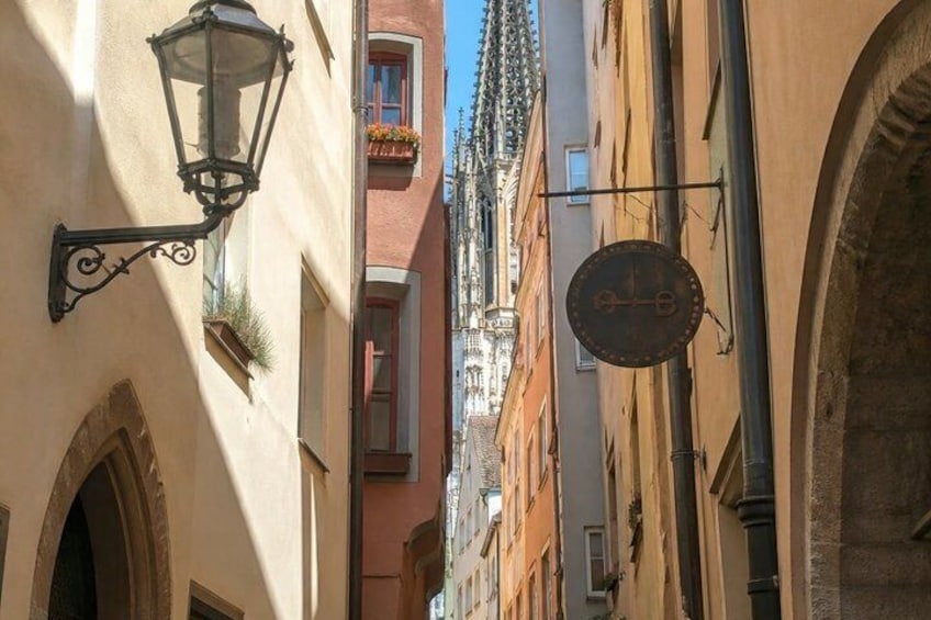 A narrow street with buildings, a street lamp, and a clock. 5