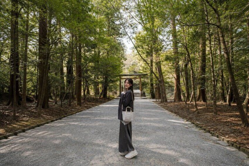 A person standing on a paved path in a forested area with trees on both sides. 3