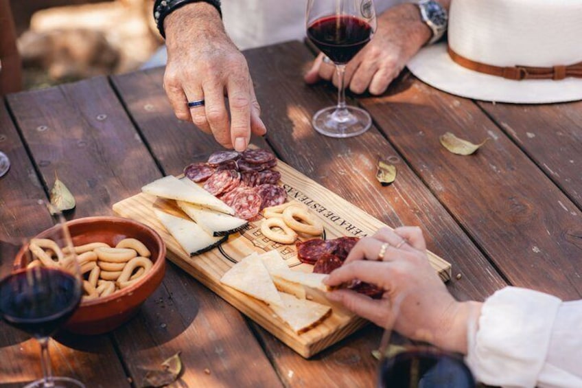 A wooden table with a charcuterie board, a bowl of pretzels, and a glass of red wine. 4