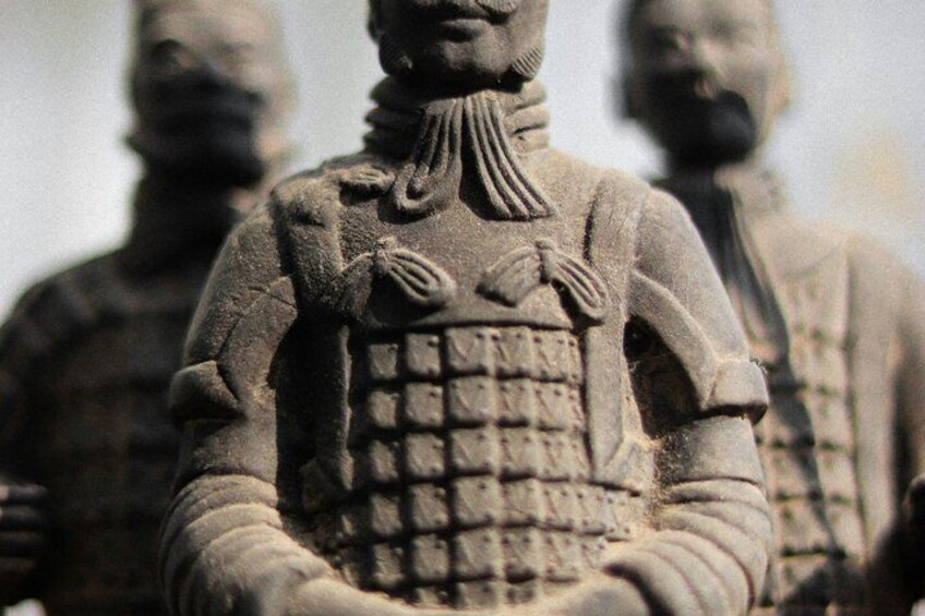 A terracotta statue of a soldier with a detailed uniform, standing in a row with others. 3