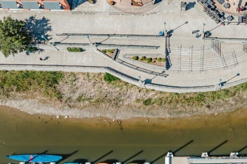 An aerial view of a riverside promenade with a curved walkway, seating areas, and a bridge. 4