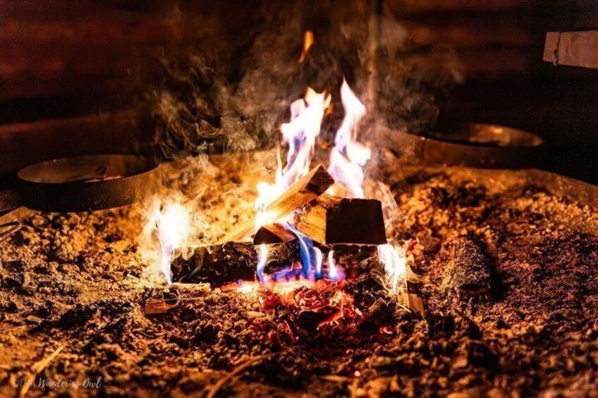 A campfire with logs and flames, surrounded by charred wood and ash. 2