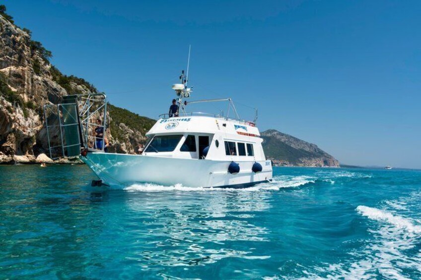 A white boat with blue accents on a turquoise sea, surrounded by rocky cliffs and a clear sky. 3