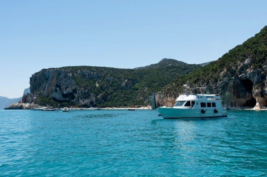 A boat on turquoise water, a rocky coastline, and a mountainous backdrop. 2