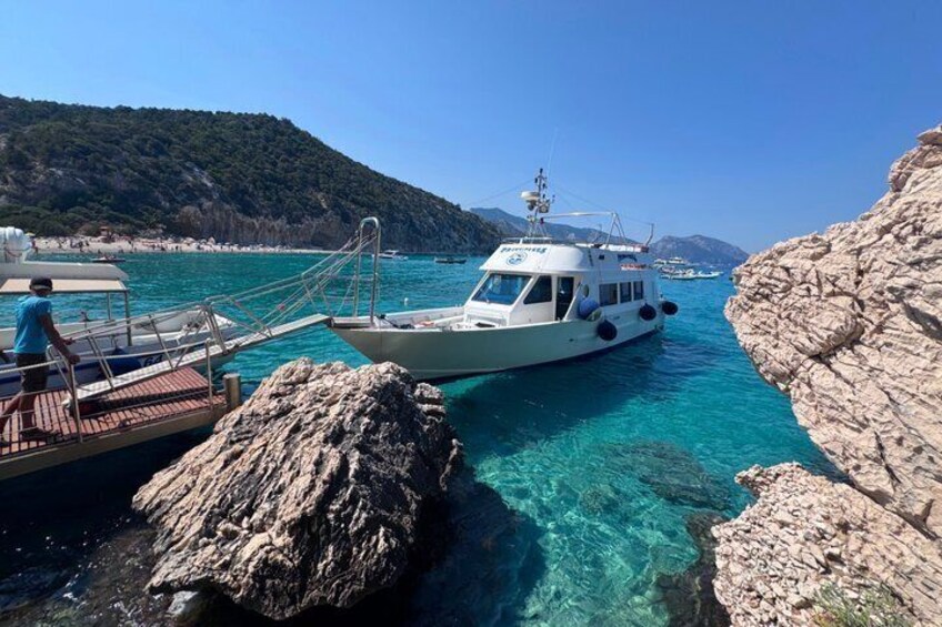A boat docked at a rocky shoreline with clear turquoise water. 1