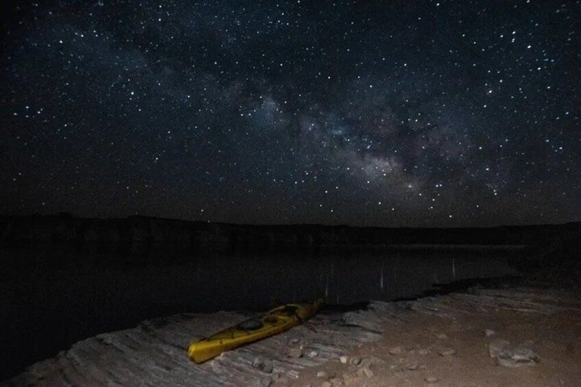A starry night sky over a desert landscape with a yellow object on the ground. 2